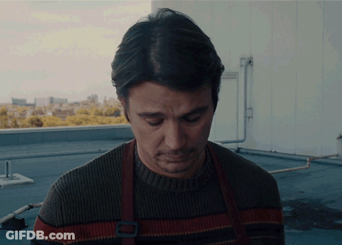 A Man In A Sweater And Apron Looks Down GIF