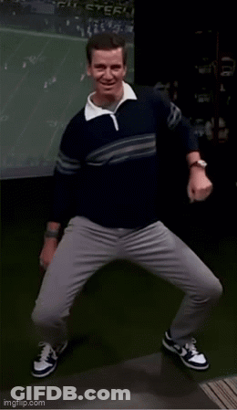 A Man In A Sweater And Gray Pants Is Dancing In Front Of A Screen . GIF