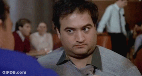 A Man In A Sweater And Tie Is Looking At Another Man . GIF