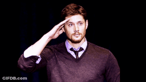 A Man In A Sweater And Tie Salutes In Front Of A Black Background GIF