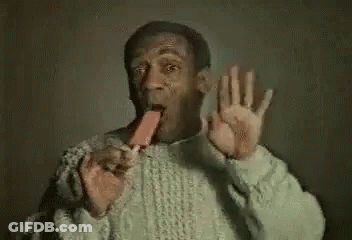A Man In A Sweater Is Eating An Ice Cream Bar And Waving . GIF
