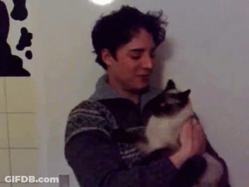A Man In A Sweater Is Holding A Cat In His Hands GIF