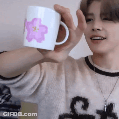 A Man In A Sweater Is Holding A Mug With A Pink Flower On It GIF
