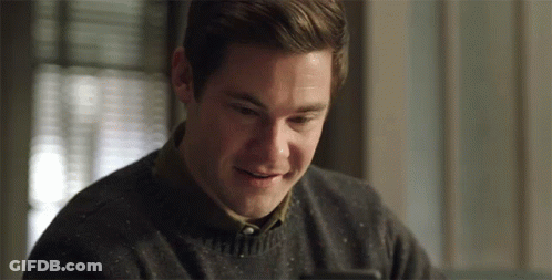A Man In A Sweater Is Smiling And Looking At His Phone GIF