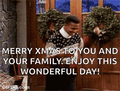 A Man In A Sweater Is Standing In Front Of A Door With A Wreath On It And Says Merry Xmas GIF