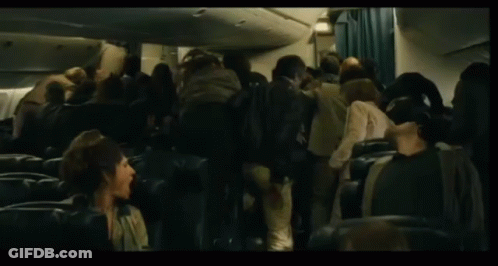A Man In A Sweater Is Walking Through A Crowd Of People On An Airplane GIF