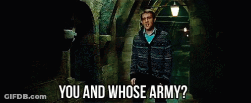 A Man In A Sweater Says " You And Whose Army " In A Dark Hallway GIF
