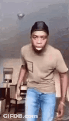 A Man In A T-Shirt And Jeans Is Standing In A Living Room . GIF
