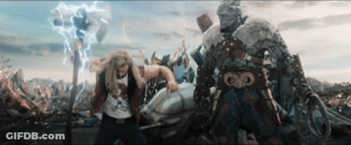 A Man In A T-Shirt That Says ' Thor ' On It Stands Next To Another Man GIF