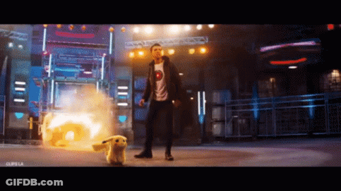 A Man In A T-Shirt With A Smiley Face On It Is Standing Next To A Pikachu GIF
