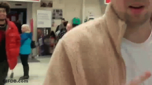 A Man In A Tan Jacket Is Standing In A Crowd GIF