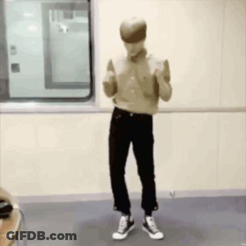 A Man In A Tan Shirt And Black Pants Is Standing In A Room . GIF