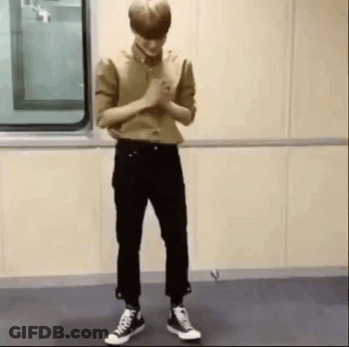 A Man In A Tan Shirt And Black Pants Is Standing In Front Of A Window . GIF