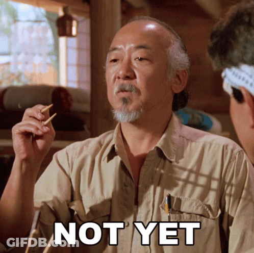 A Man In A Tan Shirt Holds Chopsticks In His Hand And Says " Not Yet " GIF