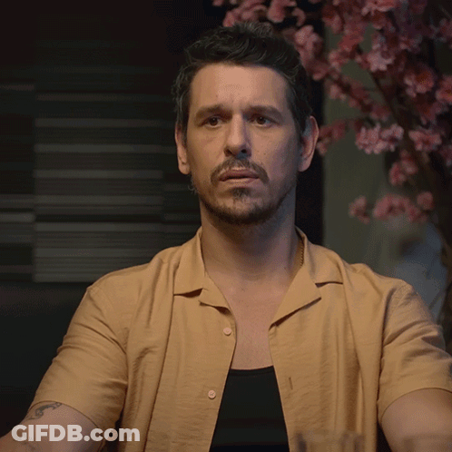 A Man In A Tan Shirt Holds Up His Hand GIF