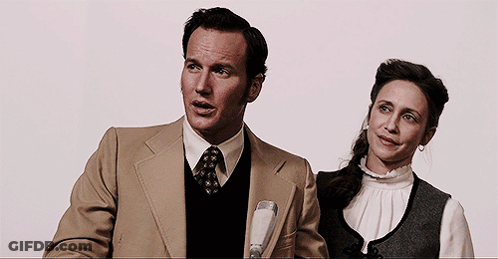 A Man In A Tan Suit And Tie Stands Next To A Woman In A White Shirt GIF
