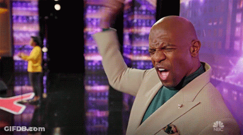 Man In Tan Suit Raising Fist In Front Of NBC Sign GIF