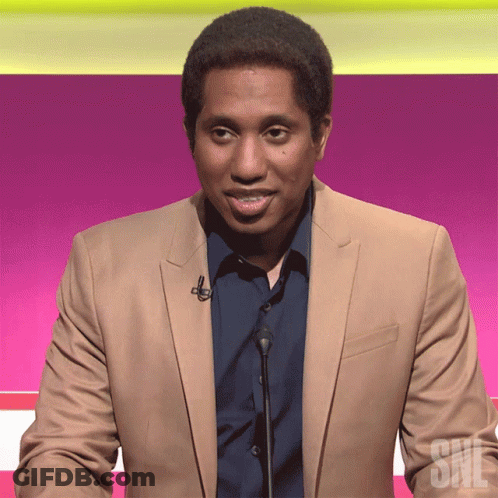 A Man In A Tan Suit Stands In Front Of A Microphone With The Letters Snl On The Bottom GIF