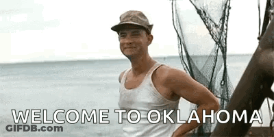 A Man In A Tank Top And Hat Is Standing On A Boat In The Ocean And Says `` Welcome To Oklahoma '' . GIF