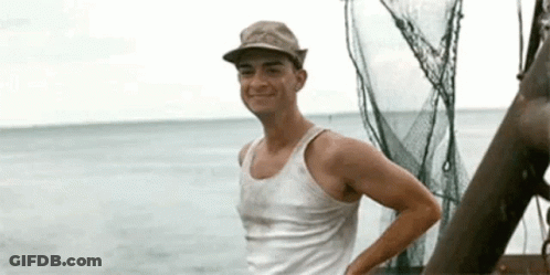 A Man In A Tank Top And Hat Is Standing On A Boat In The Water . GIF