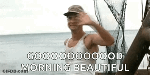 A Man In A Tank Top And Hat Is Waving At The Camera While Standing On A Boat In The Ocean . GIF