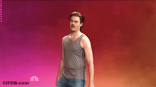 A Man In A Tank Top And Jeans Is Standing On A Stage . GIF