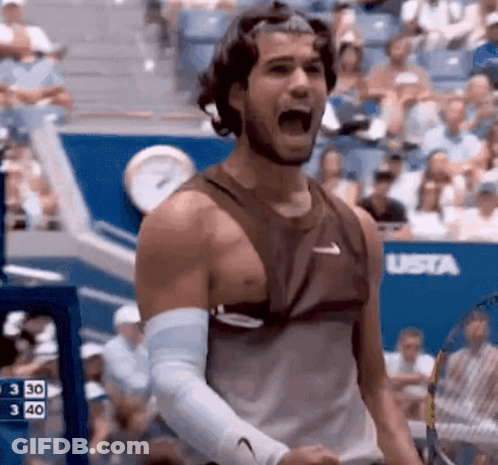 A Man In A Tank Top Is Holding A Tennis Racquet And Shouting . GIF