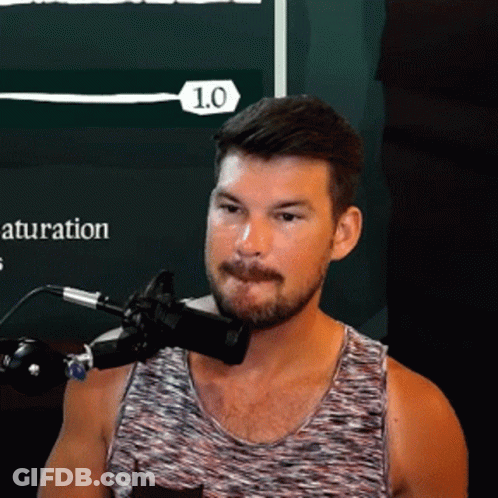 A Man In A Tank Top Is Speaking Into A Microphone With The Number 1.0 On The Bottom Right GIF