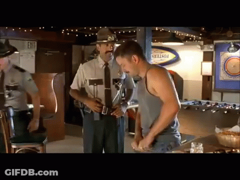 A Man In A Tank Top Is Standing In Front Of A Police Officer In A Bar GIF