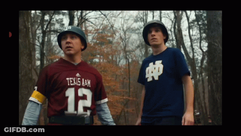 A Man In A Texas A & M Jersey Stands Next To Another Man GIF