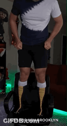 A Man In A Tie Dye Shirt And Black Shorts Is Standing On A Chair With The Words Just For You Brooklyn Above Him GIF