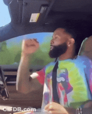 A Man In A Tie Dye Shirt And Tie Is Driving A Car GIF