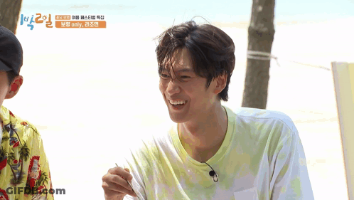 A Man In A Tie Dye Shirt Is Smiling In Front Of A Sign That Says ' Emily ' On It GIF