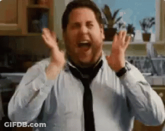 A Man In A Tie Is Laughing With His Hands In The Air In A Kitchen . GIF