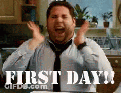 A Man In A Tie Is Sitting At A Table With His Hands In The Air And The Words First Day Written Below Him . GIF
