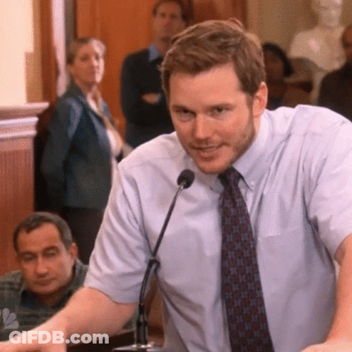 A Man In A Tie Is Speaking Into A Microphone In Front Of A Crowd GIF