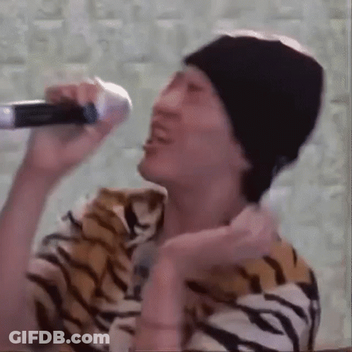 A Man In A Tiger Print Shirt Is Singing Into A Microphone While Wearing A Beanie . GIF
