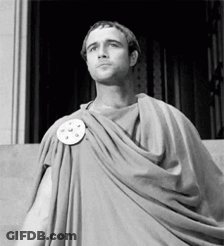 A Man In A Toga Is Standing In Front Of A Building . GIF