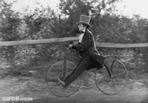 A Man In A Top Hat And Bow Tie Is Riding A Bicycle . GIF