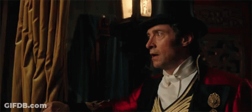 A Man In A Top Hat And Bow Tie Is Standing In A Dark Room . GIF