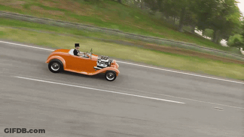A Man In A Top Hat Drives An Orange Car On A Road GIF