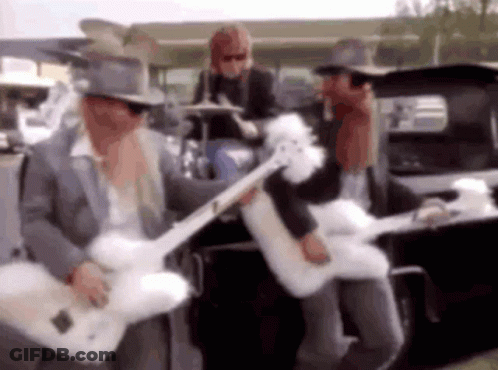 A Man In A Top Hat Is Playing A Guitar In Front Of A Car . GIF