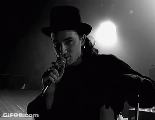 A Man In A Top Hat Is Singing Into A Microphone In A Black And White Photo GIF