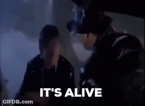 A Man In A Top Hat Is Talking To Another Man In A Dark Room And The Words It 'S Alive Are Visible . GIF