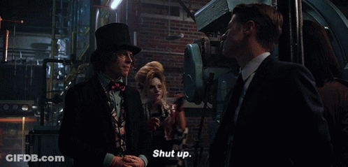 A Man In A Top Hat Says Shut Up In Front Of A Woman In A Striped Jacket GIF