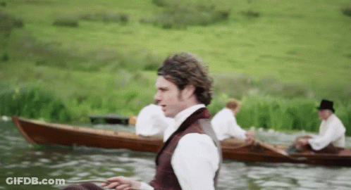 A Man In A Top Hat Sits In A Boat On A Lake GIF