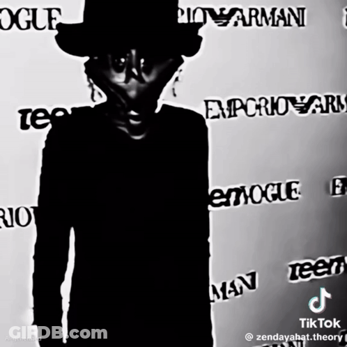 A Man In A Top Hat Stands In Front Of A Wall That Says Vogue GIF