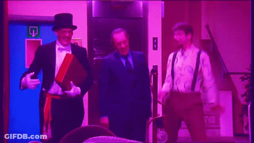 A Man In A Top Hat Stands Next To Two Other Men In Suits GIF