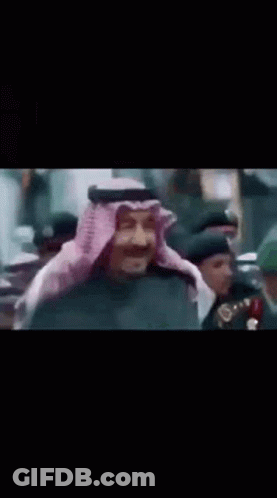 A Man In A Traditional Arabic Costume Is Standing In Front Of A Crowd Of People . GIF