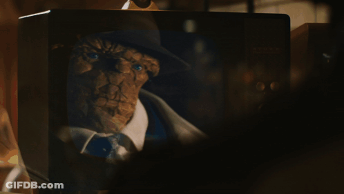 A Man In A Trench Coat And Hat Is Walking Down A Dark Street GIF